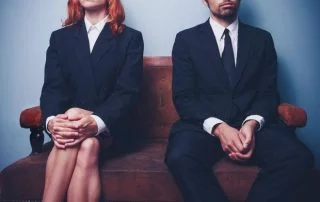 Suited woman and man sat on bench with arms crossed