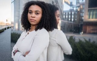 Black woman leaning against building with arms crossed