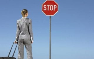 Woman looks at STOP sign while rolling suitcase