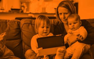 Mother holding her two children on a couch, while eldest hold a tablet