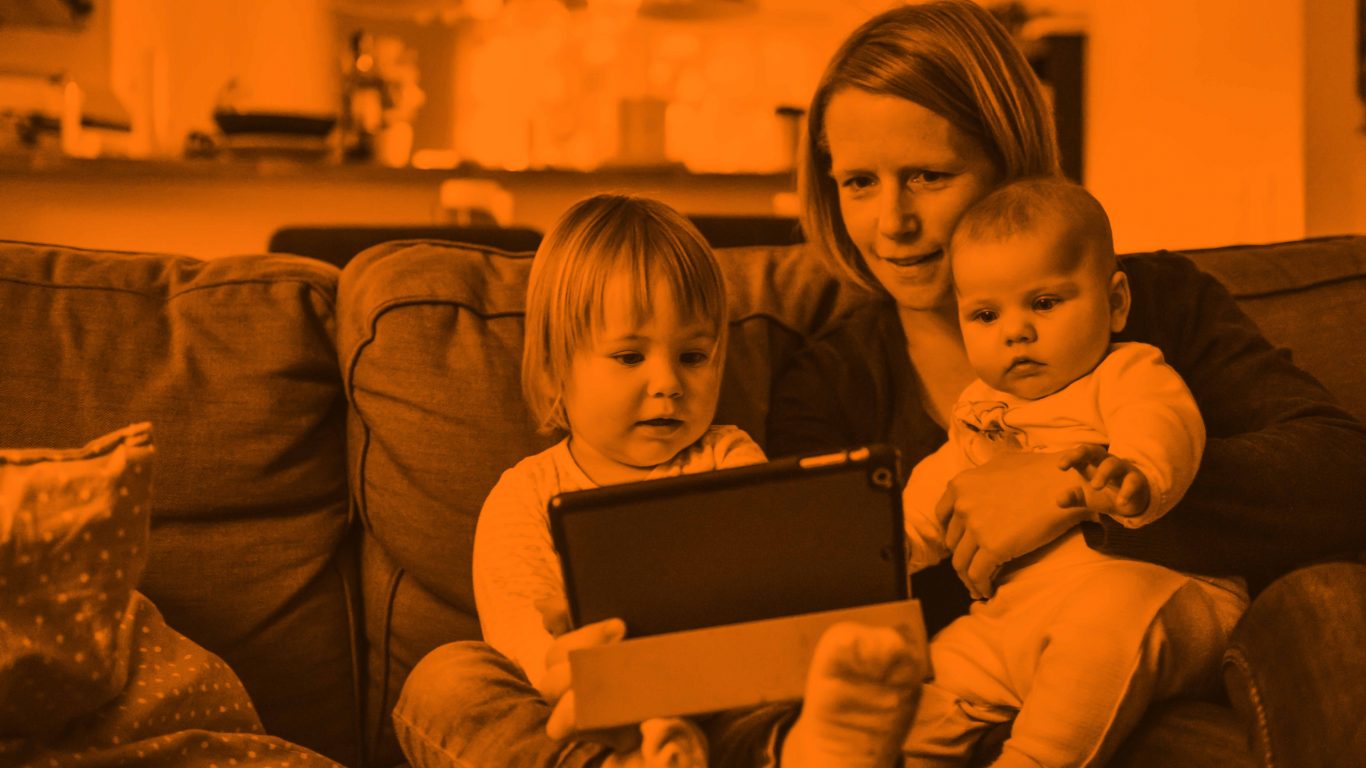 Mother holding her two children on a couch, while eldest hold a tablet