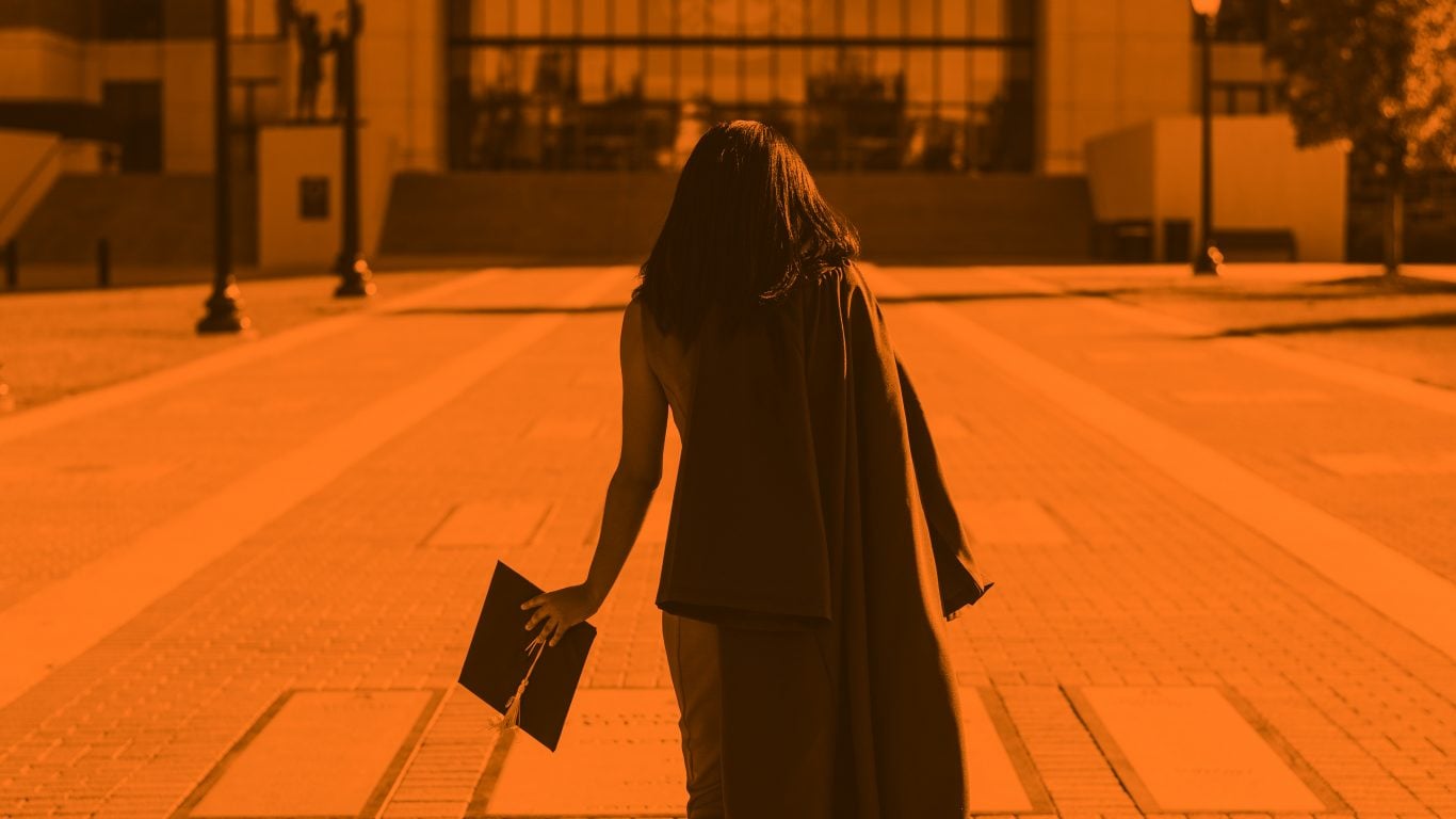 Graduate walking away from camera with convocation hat in hand