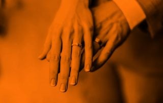 A woman's hand overtop of a man's hand as they both display their wedding bands