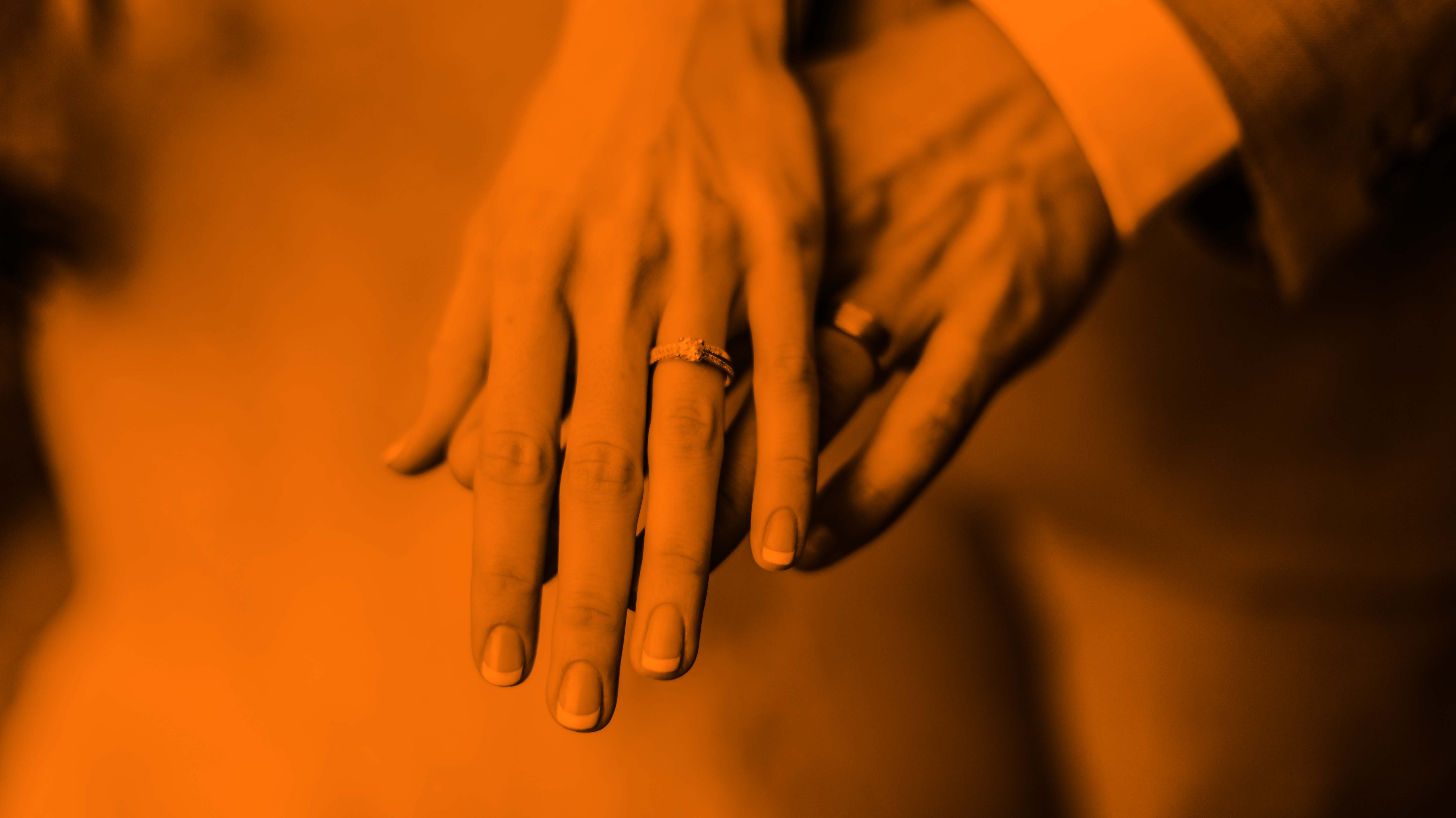 A woman's hand overtop of a man's hand as they both display their wedding bands