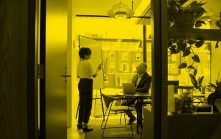 Woman standing doing a presentation in office with one seated male attendee