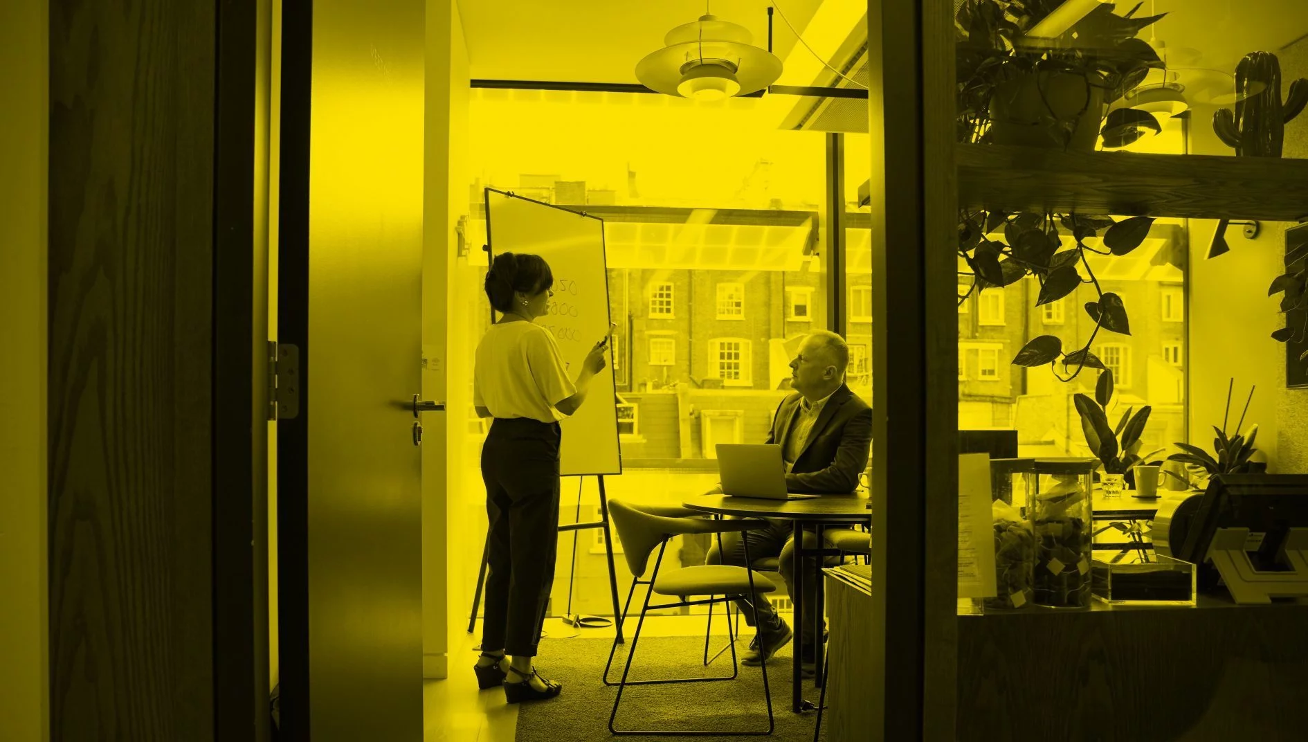 Woman standing doing a presentation in office with one seated male attendee