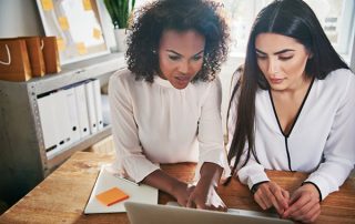 Two women sat at a table reviewing a laptop