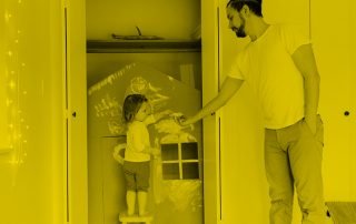 Father handing paintbrush to daughter painting play house