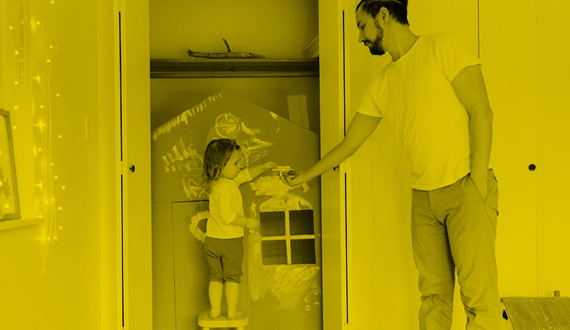 Father handing paintbrush to daughter painting play house