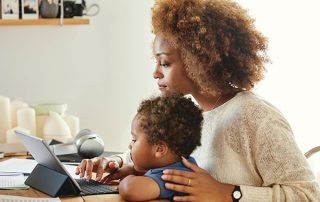 Woman holding child while working on tablet