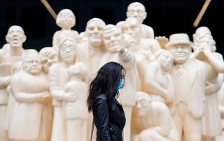 Woman with mask walking past series of statues