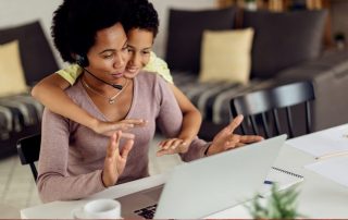 Woman sat at home desk with son wrapping his arm around her