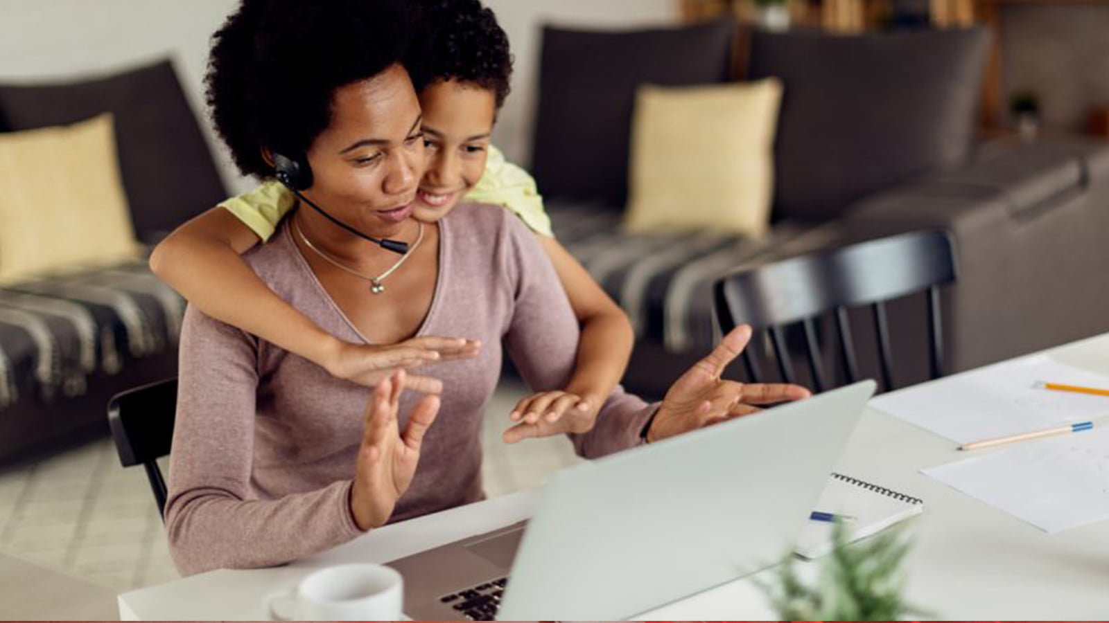 Woman sat at home desk with son wrapping his arm around her