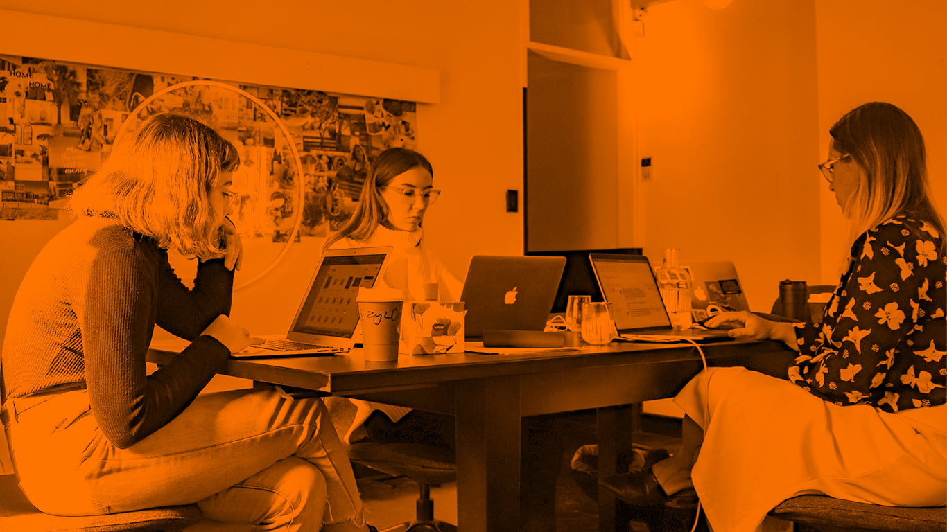 Office with three women sat at desk with their laptops