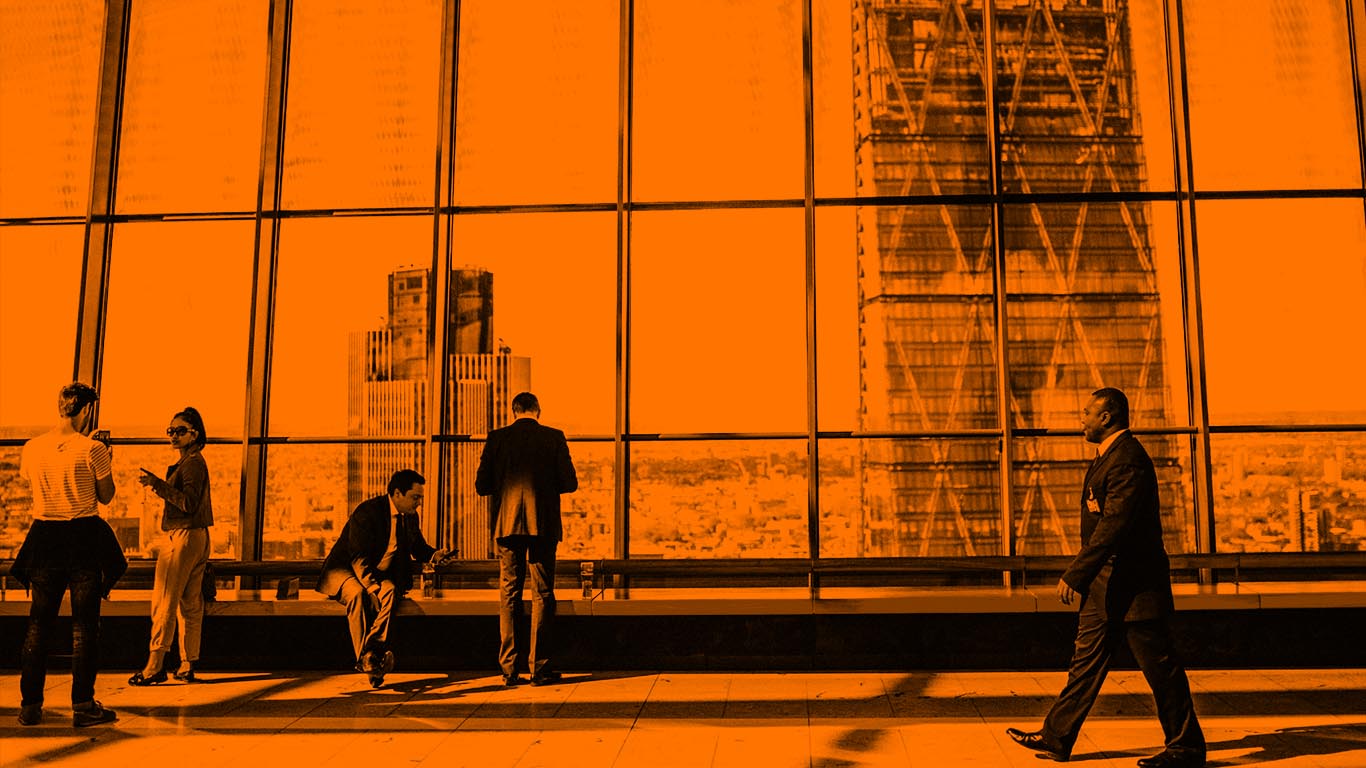 Long shot of building hallway with populated with several people, overlooking cityscape.