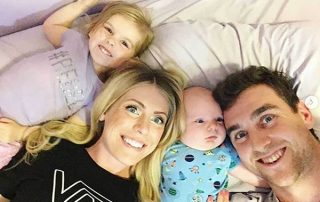 Family of four laid on bed looking up at camera