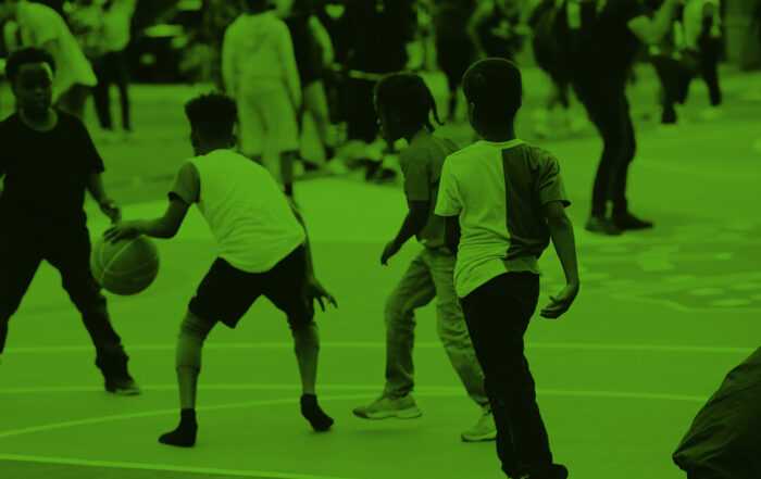 Four Black children in a schoolyard play basketball