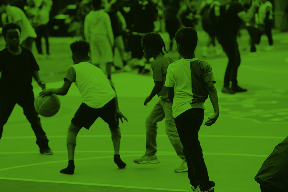Four Black children in a schoolyard play basketball