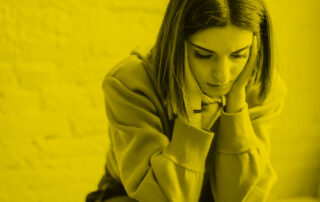 A woman with short hair sits, looking down with her head in her hands.