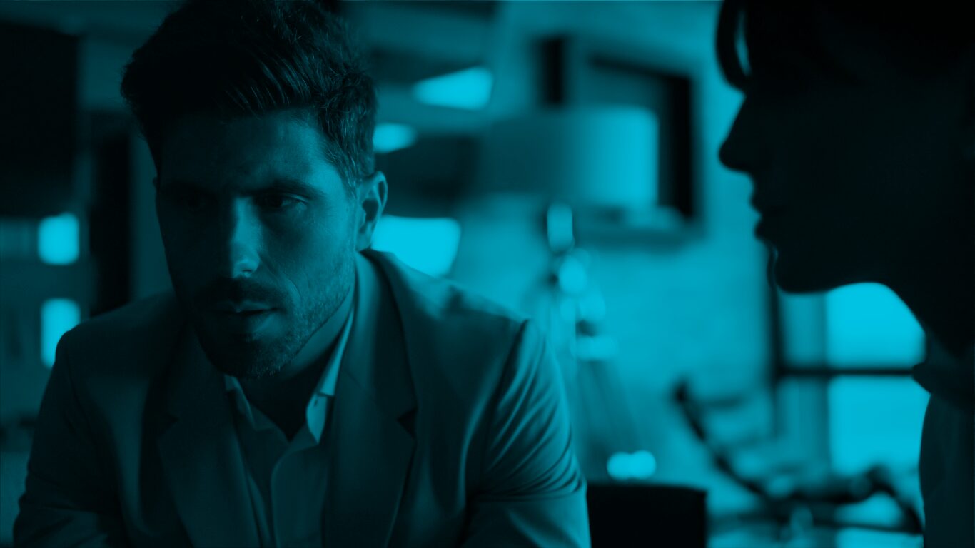 A man at work looks to the side with a serious expression. In front of him is a woman's silhouette.