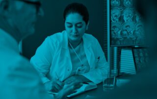 A woman doctor writes notes in front of two men colleagues.